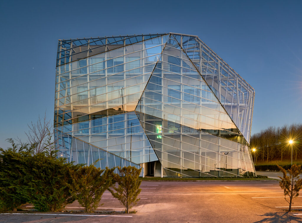 Fotografía nocturna de arquitectura exterior del edificio E8 en el Parque Tecnológico de Álava, con fachada de vidrio, geometría angular e iluminación al atardecer, realizada por Zigor Astigarraga, fotógrafo de arquitectura e interiorismo en Durango, Bizkaia.